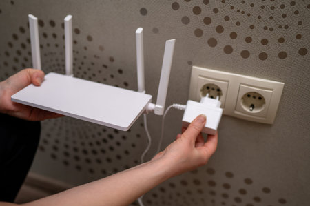 A person is connecting a wireless internet router to the electricity supply by plugging the power...