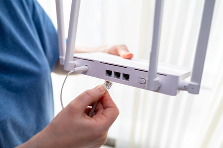 Close-up of a person in a blue shirt connecting a network cable into a wireless router. This shot...