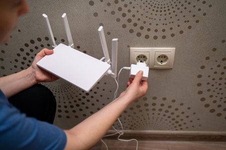 A person is connecting a wireless internet router to the electricity supply by plugging the power...