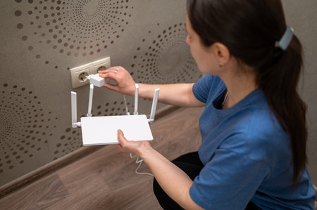 A person is connecting a wireless internet router to the electricity supply by plugging it into a...