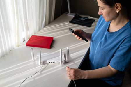 A person is holding a phone and setting up a wireless internet router with antennas on a white desk....
