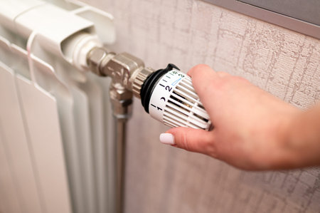 A close up shot of a hand turning a thermostatic radiator valve on a central heating system to regulate heat levels and improve energy efficiency in a domestic living space during the winter seasonの写真素材