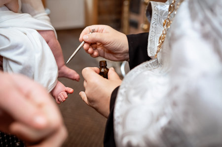 A close up shot of a priest hands holding a small bottle and an applicator brush to anoint a newborn...