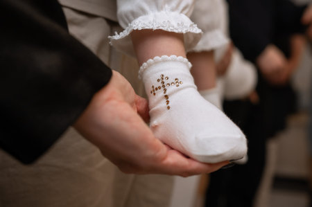 Close up of newborn infant leg in parent hand wearing christening socks with embroidered crucifix...