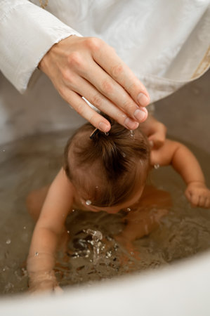 Close up of priest hand and water drops on infant head during christening ritual in church cathedral...