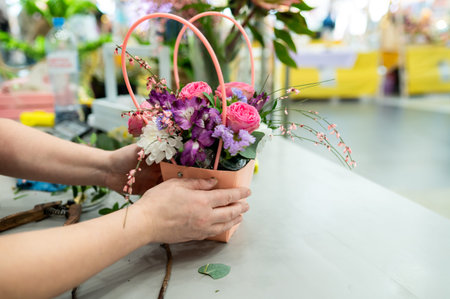 Close up of a flower shop worker placing pink roses and white chrysanthemums with purple statice...