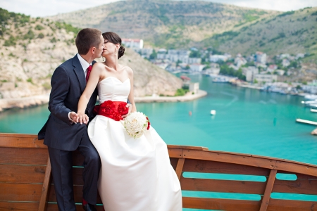 Young couple in love the bride and groom with a bouquet posing on the background beautiful mountains and bays of the wedding day in the summer  Enjoying a moment of happiness and love の写真素材