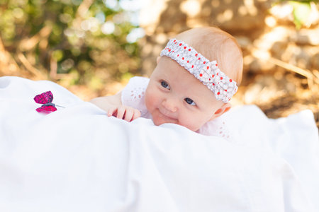 Little beautiful baby posing on a white blanket and look at the blue butterfly in summer park  A...