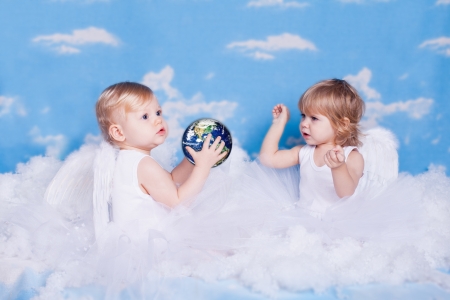 Two small children in the form of angels in the clouds playing with a toy  Planet Earth   studio photographの写真素材