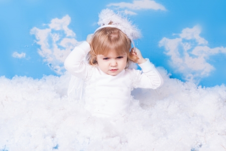 Beautiful baby girl with angel wings in white clothes posing on a background of the sky with clouds - decorated in the style of a little angel in the clouds  A series of photos in my portfolio の写真素材