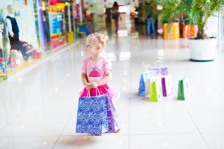 Elegant little girl in a big shopping center posing on the background shop windows の写真素材