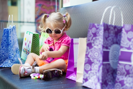 Elegant little girl posing on a big sofa in the mall on the background shop windows の写真素材