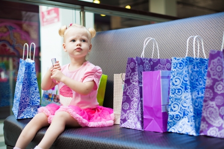 Elegant little girl posing on a big sofa in the mall on the background shop windows の写真素材