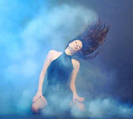 Beautiful young woman with perfect hair posing sitting around shaking his head in the smoke  Studio shot の写真素材