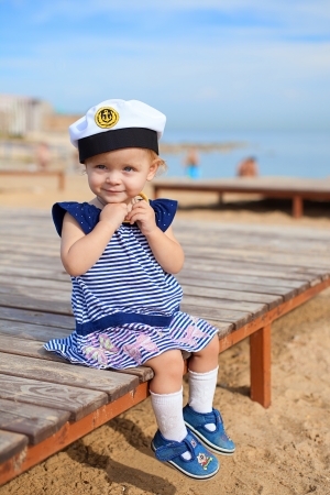 Cute little girl is 1 year old, posing on the beach by the sea on a background of blue sky, sitting の写真素材