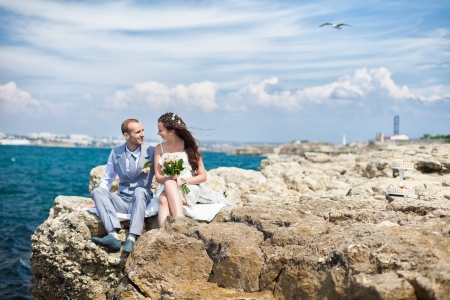Happy pregnant bride and groom holding wedding bouquet posing against the sea  The groom tenderly embraces the pregnant belly of his wife の写真素材