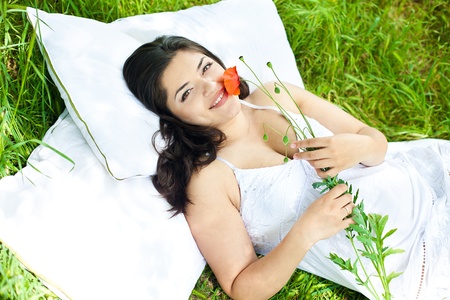 portrait of beautiful young woman laying on a green grass with flower in a parkの写真素材