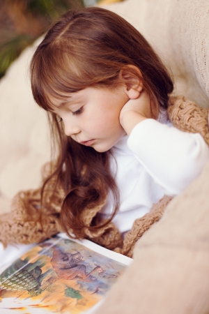 beauty child in shawl reading a book while lying on the couch の写真素材