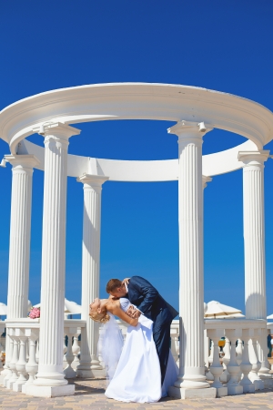 Young couple in love bride and groom posing with white columns on the background of bright blue sky  Wedding day in summerの写真素材