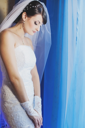young beautiful bride wear in dress and veil standing by the windowの写真素材