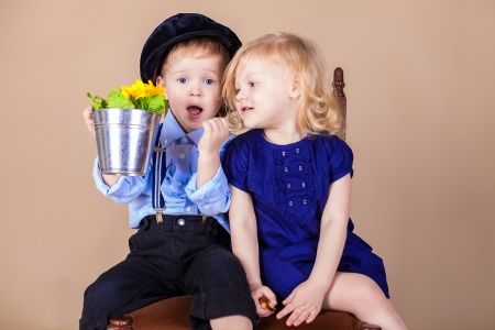 Funny kids, happy little boy giving a cute girl bouquet of yellow spring flowers. Series in studioの写真素材