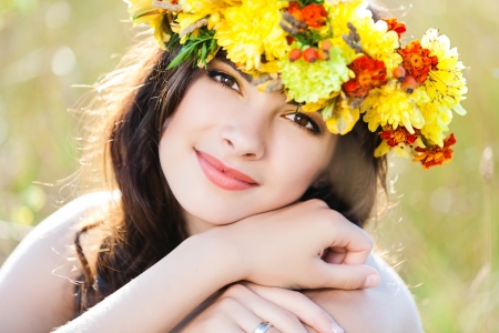 Closeup portrait of beautiful young woman with flower wreath on her head against summer fieldの写真素材