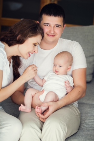 mother and father playing with their cute baby on the couch at homeの写真素材
