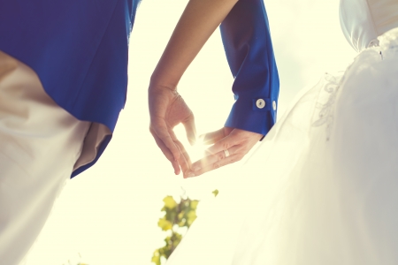 wedding couple hands touching fingers in the shape of hearts. Bright light of the sun on .