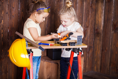 Two little girls making very interesting creations with tools and wood at homeの写真素材