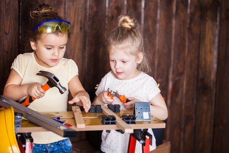 Two little girls making very interesting creations with tools and wood at homeの写真素材