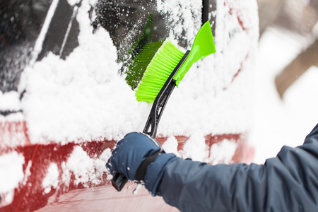 Transportation, winter, weather, people and vehicle concept - man cleaning snow from car with brushの写真素材