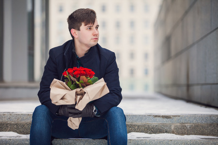 Waiting for his girlfriend. Handsome young man holding bouquet of flowersの写真素材
