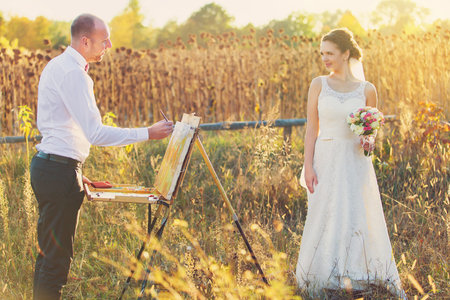 Groom paints a portrait of his beloved bride. Newly married wedding couple in a vintage setting. Sunsetの写真素材