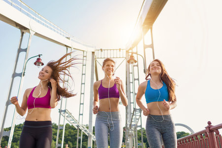 Three sportive pretty women enjoying their run - on city bridge at sunset. Sporty friends portrait