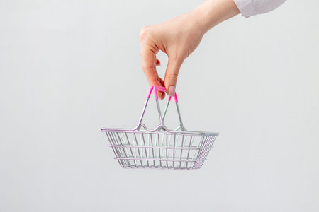 Close-up of a womans hand horizontally holding a toy small metal shopping basket with a pink plastic...