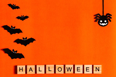 Halloween lettering on orange background with black paper silhouettes, bats, pumpkin, spider. The...