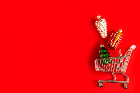 A full shopping basket of different glass and glossy Christmas tree toys on a red background. Christmas toys are spilled out of the stores basket. online shopping, Christmas shopping, black Fridayの写真素材