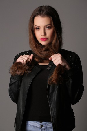 Teen in a studded leather jacket holding her hair, high fashion look, perfect make-up, beautiful girl, smiling girl, isolated, looking into the camera, clear skin,big lips, model in studio, close up, white backgroundの写真素材