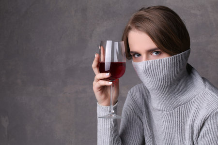 Girl with wine hiding her face by collar, girl with wineglass, high fashion look, beautiful girl, blonde girl, isolated, model in studio, long hair, close up, gray backgroundの写真素材