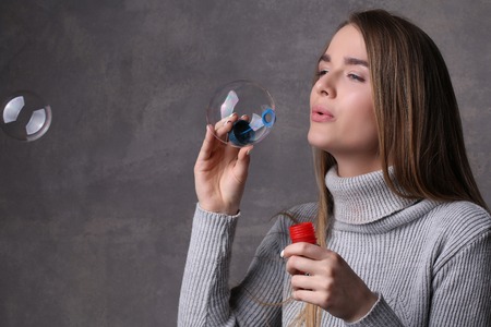 Girl blowing bubbles, bubble blower , high fashion look, beautiful girl, blonde girl, isolated, model in studio, long hair, close up, gray backgroundの写真素材