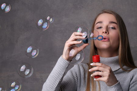 Girl in turtleneck blowing bubbles, bubble blower , high fashion look, beautiful girl, blonde girl, isolated, model in studio, long hair, close up, gray backgroundの写真素材