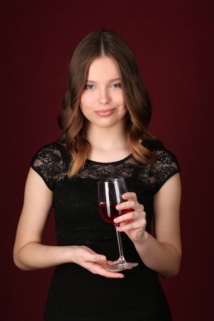Girl in dress holding wineglass, girl with wineglass, high fashion look, beautiful girl, brunette girl, isolated, model in studio, long hair, close up, dark red backgroundの写真素材