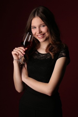Portrait of model with wineglass, girl with wineglass, high fashion look, beautiful girl, brunette girl, isolated, model in studio, long hair, close up, dark red backgroundの写真素材