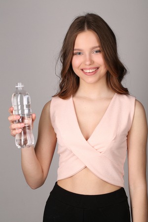 Girl with bottle of water, high fashion look, healthy lifestyle, beautiful girl, smiling girl, isolated, perfect make-up, big lips, model in studio, close up, gray backgroundの写真素材