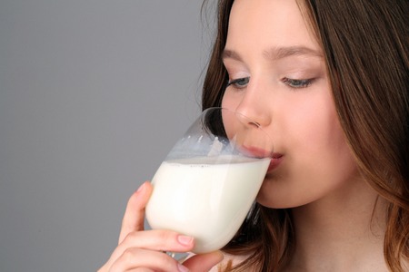 Girl drinking milk from a wine glass, high fashion look, healthy lifestyle, beautiful girl, smiling girl, isolated, perfect make-up, big lips, model in studio, close up, gray backgroundの写真素材