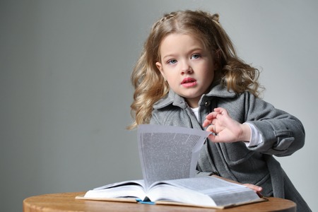 Portrait of little girl in coat with a book, happy childhood, high fashion look, little girl, happy family, cute baby, beautiful girl, blonde girl, isolated, baby in studio, long hair, close up, gray backgroundの写真素材