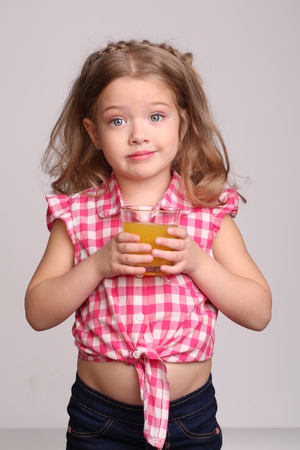 Lady in plaid shirt with a glass of juice, happy childhood, little girl, happy family, fashion clothes, cute baby, blonde girl, isolated, baby in studio, gray backgroundの写真素材