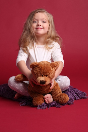 Little girl in pajamas holding bear, happy childhood, little girl, happy family, fashion clothes, cute baby, blonde girl, isolated, baby in studio, red backgroundの写真素材
