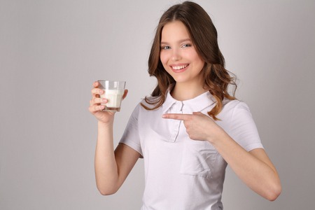 Girl points her finger at the glass of milk, girl in white T-shirt, high fashion look, healthy lifestyle, beautiful girl, smiling girl, isolated, perfect make-up, big lips, model in studio, close up, hite backgroundの写真素材