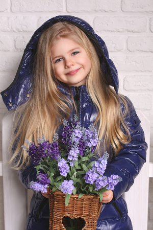 Little girl with wooden bucket of flowers, texture background, autumn theme, white brick wall, warm clothes, cute baby, blonde girl, white backgroundの写真素材
